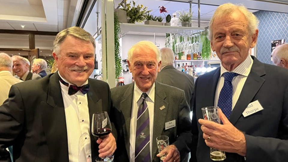 Three people wearing suits, standing together and holding drinks