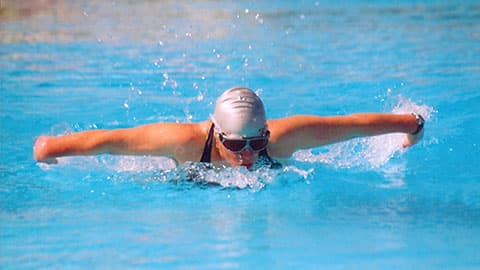 Dr Julie Bradshaw MBE in a swimming pool doing butterfly stroke.