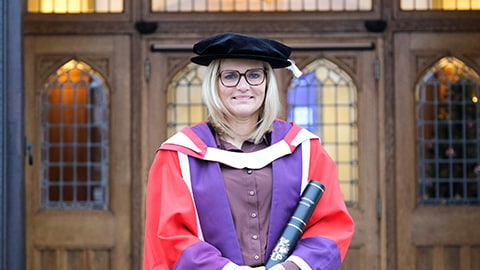 Sarina Wiegman standing at the front of the Hazlerigg Building wearing a graduation cap and red gown