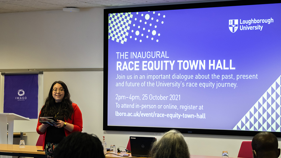 Dr Angela Martinez-Dy welcomes attendees to the Race Equity Town Hall with a large screen showing an introductory slide behind her