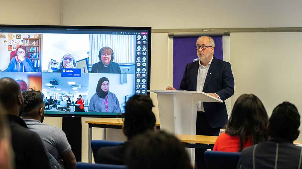 Professor Nick Jennings standing at a lectern addresses the Race Equity Town Hall with a screen showing a 'Teams' session alongside him