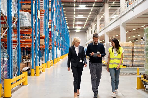 Three workers walking together in a warehouse, looking at a tablet computer.