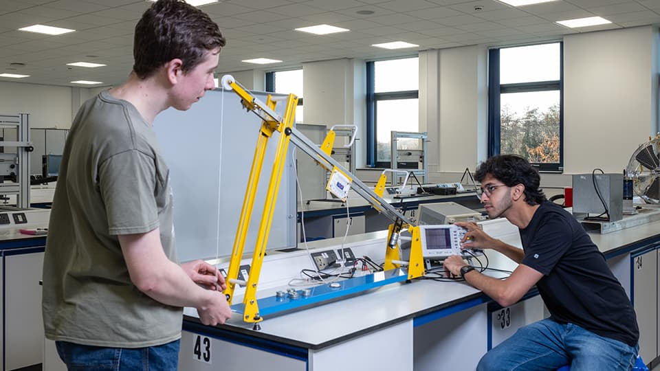 Two students in engineering lab working with mechanical engineering equipment