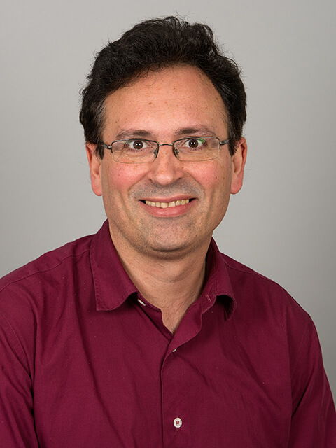 Headshot of Gianfranco smiling at the camera with a grey background.