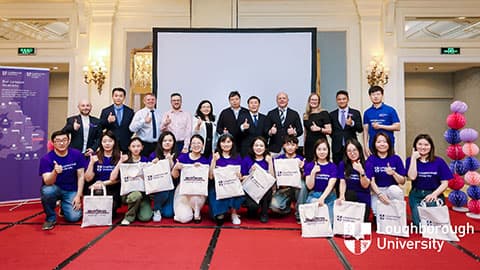 A group shot of alumni wearing Loughborough University t-shirts and prospective students along with other attendees standing and smiling at the camera at Loughborough University's Beijing alumni event.