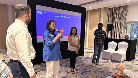 A group of three alumni standing in front of a screen that says 'Meet our alumni' talking to an audience at Loughborough University's India pre-departure event