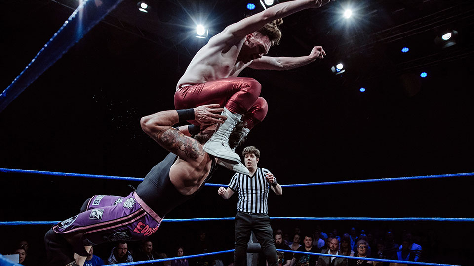 two men wrestling, referee in background