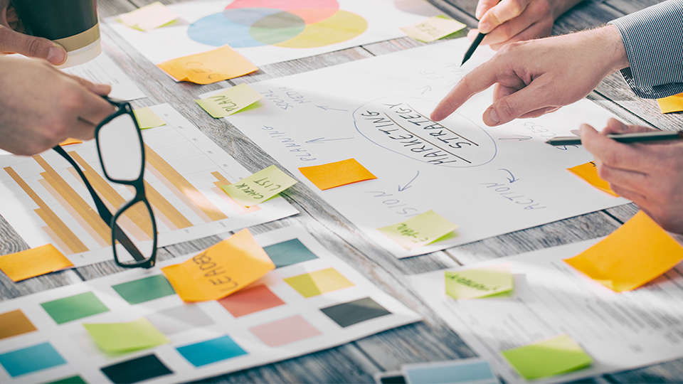 photo of a group of people working together on a business project, showing post it notes and mindmaps on paper