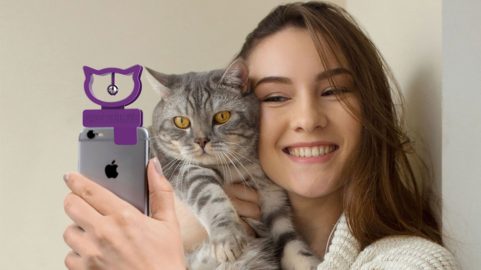 photo of cat selfie accessory clipped to a phone with a woman holding a cat and taking a selfie