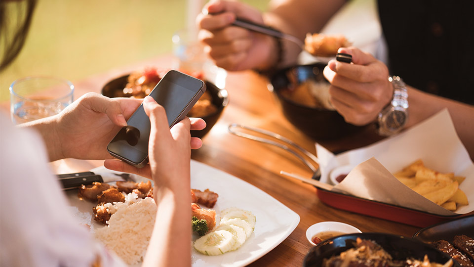 Pictured is a person on their phone while eating dinner. 