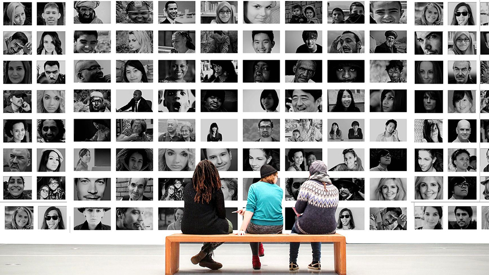 photo of three people sat on a bench staring at photos of other people