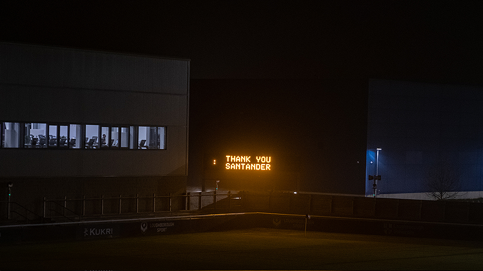 Photo of rugby pitch screen which says 'Thank you Santander' in the evening 