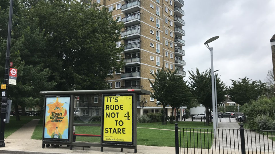 Photo of block buildings with bus stop in front showing a large, yellow Channel 4 poster to promote the Paralympic Games