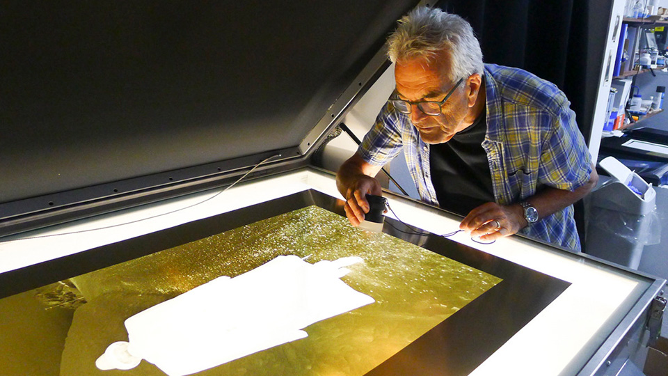 Photo of photographer Paul Hill looking over a print on a screen on a machine