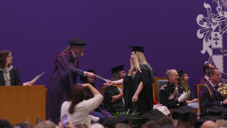 Ellie Robins accepting her degree certificate on stage at a graduation ceremony.