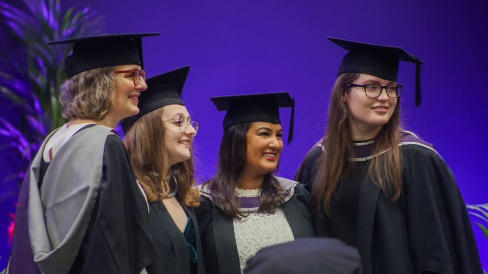 Photo of a group of women smiling stood together wearing graduation cap and gowns