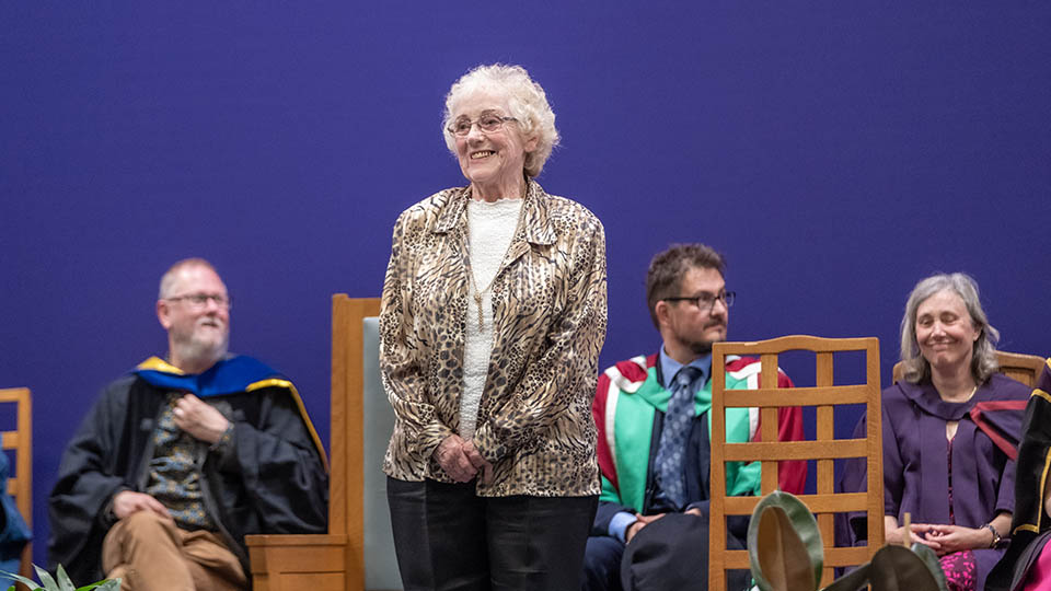 Staff member Sandra stood on stage smiling at the crowd at a graduation ceremony