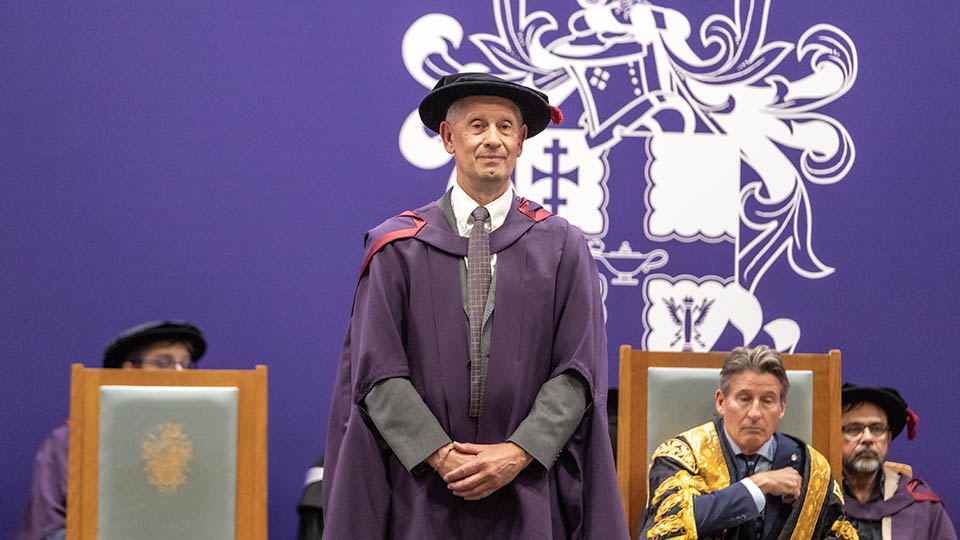 Prof Tony Thorpe stood on stage smiling with his hands together on the graduation stage