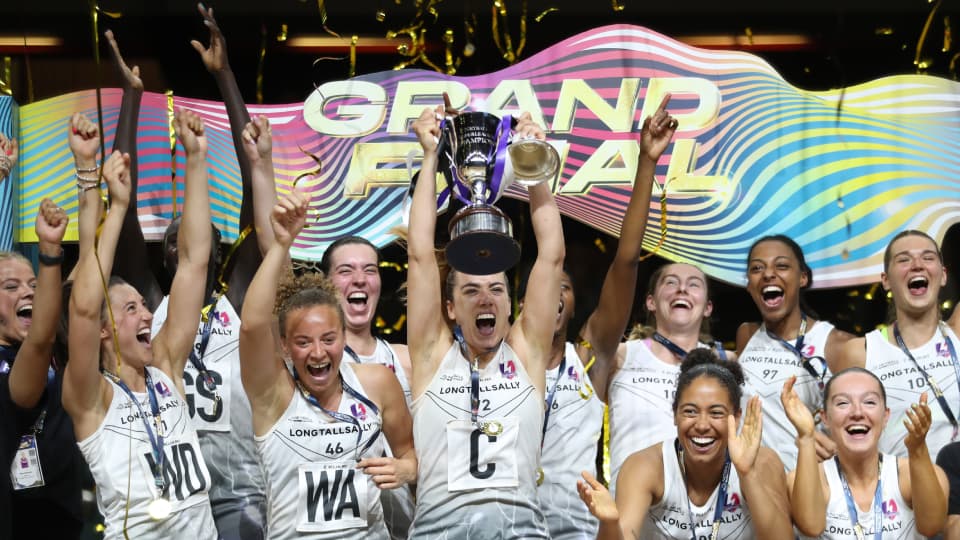 A netball player lifts a trophy aloft