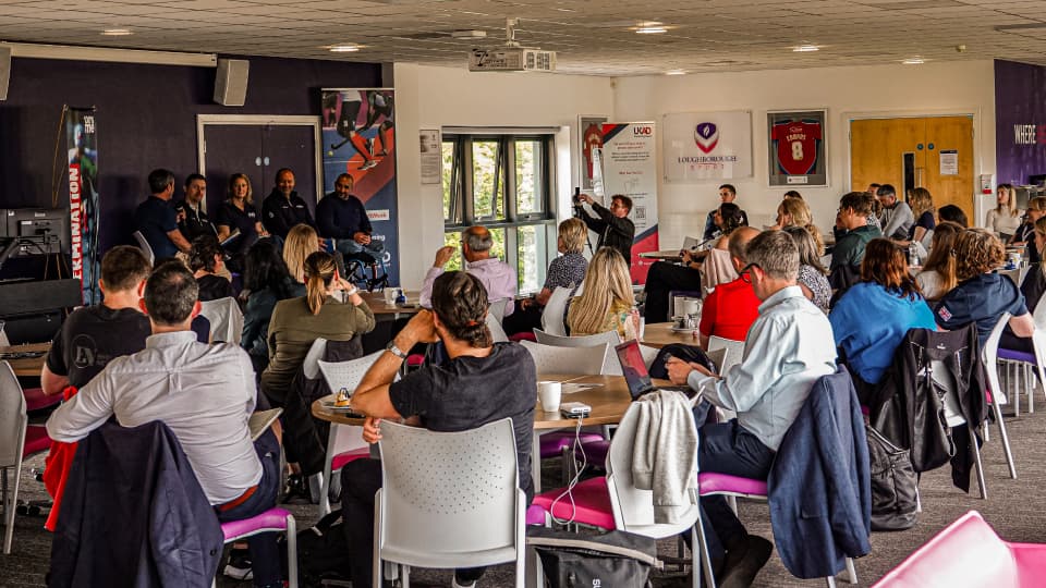 a room of people watching athletes on a stage during a panel discussion