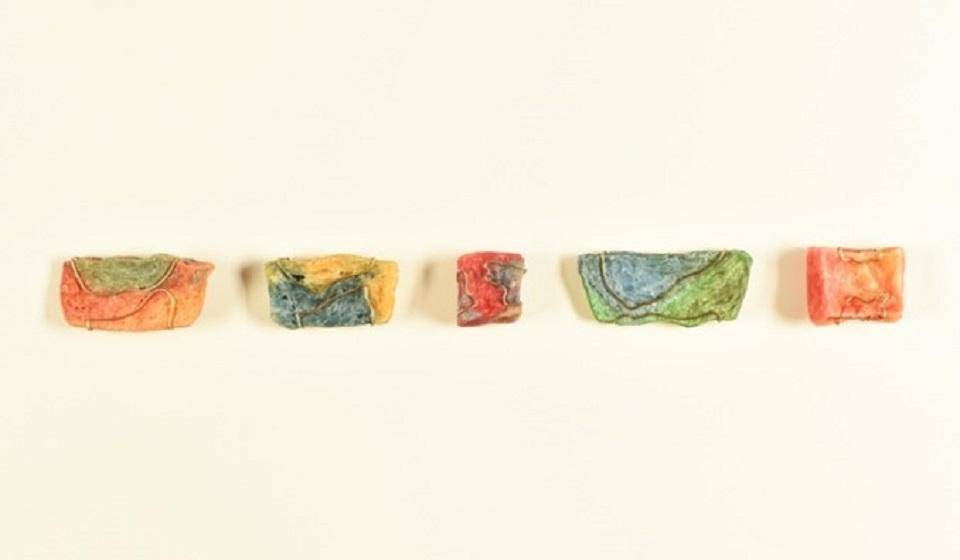 Five colourful rock shaped jewellery in a row on a cream background.