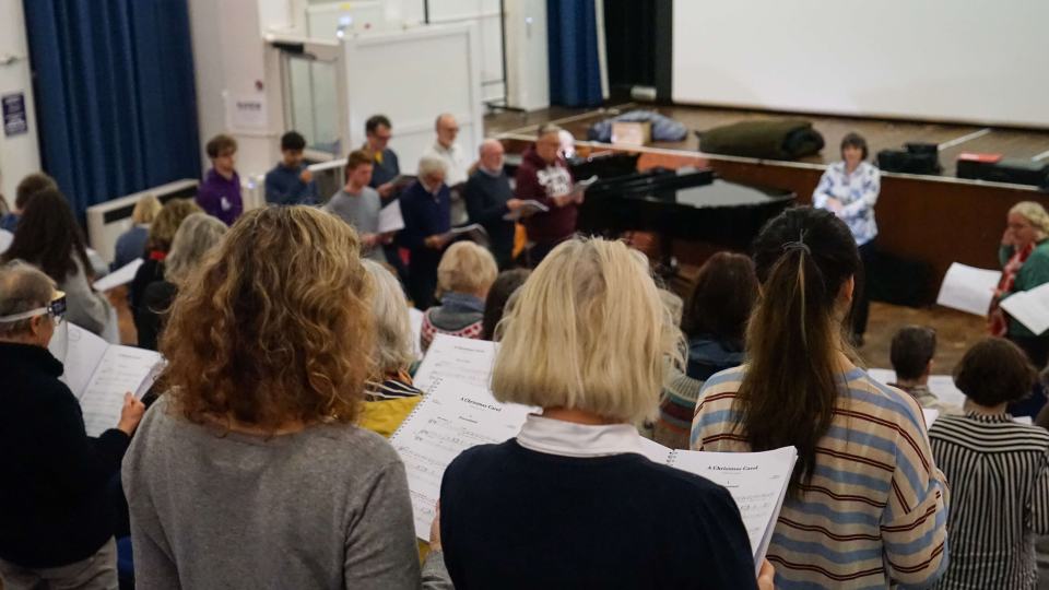 A room filled with a choir facing their conductor